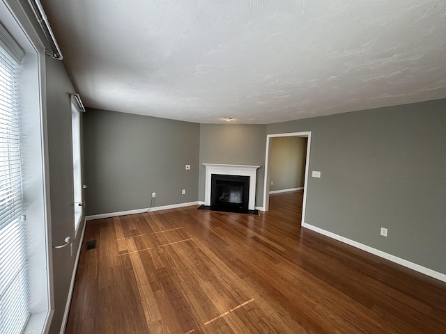 unfurnished living room with visible vents, a fireplace with flush hearth, dark wood finished floors, and baseboards