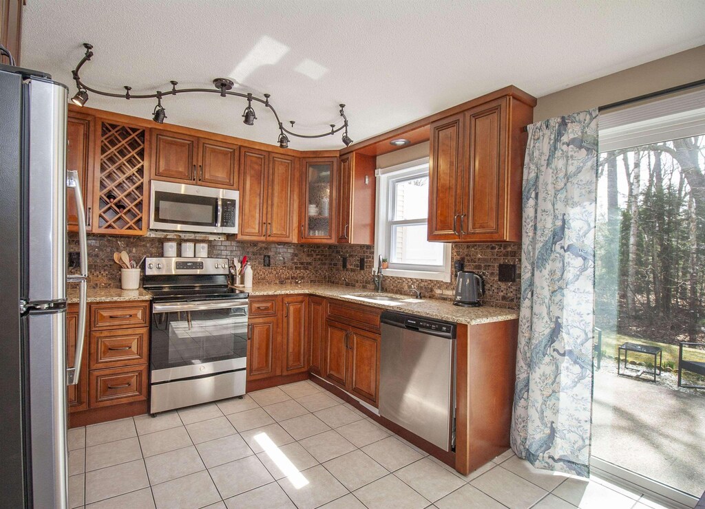 kitchen with brown cabinets, light stone countertops, a sink, stainless steel appliances, and decorative backsplash