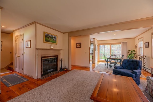 living room featuring crown molding, a fireplace with flush hearth, baseboards, and wood finished floors