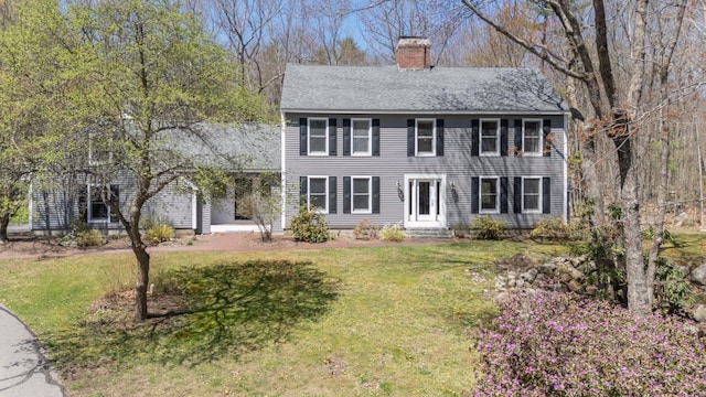 colonial-style house featuring roof with shingles, a chimney, and a front yard