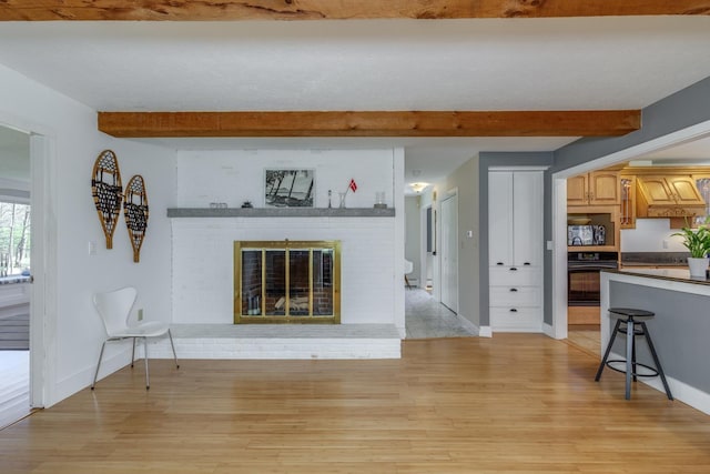 living area with baseboards, beamed ceiling, and light wood-style flooring