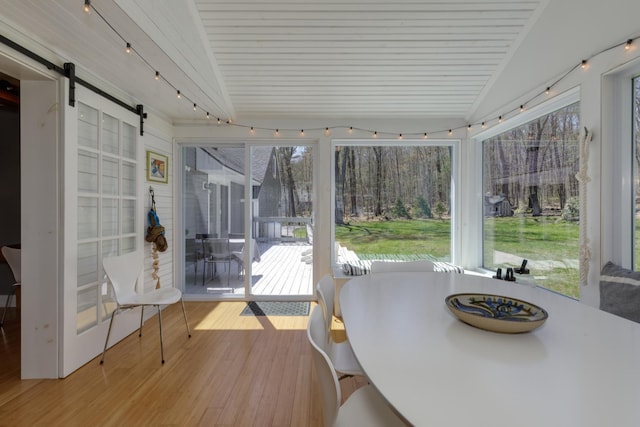 sunroom / solarium with wood ceiling, a barn door, a wealth of natural light, and hardwood / wood-style flooring