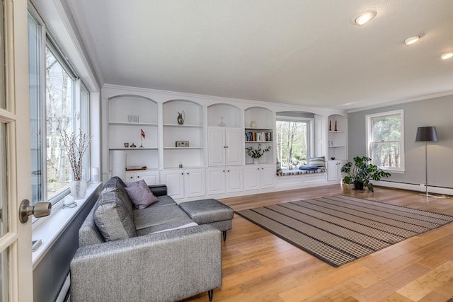 living room with built in shelves, ornamental molding, and light wood-style flooring