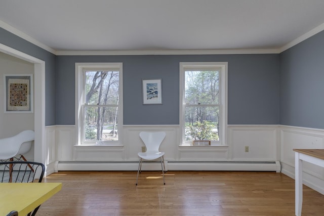 unfurnished room featuring crown molding, a baseboard heating unit, wood finished floors, and a wainscoted wall