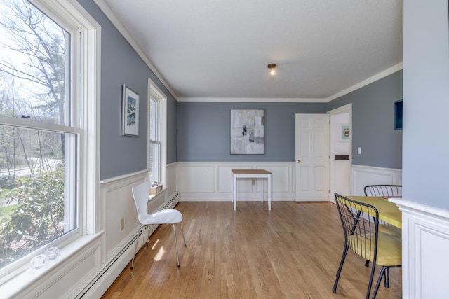 dining space featuring wood finished floors, ornamental molding, a wainscoted wall, and a baseboard radiator