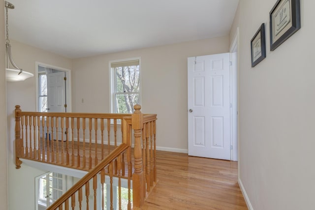 corridor featuring baseboards, an upstairs landing, and light wood-style flooring