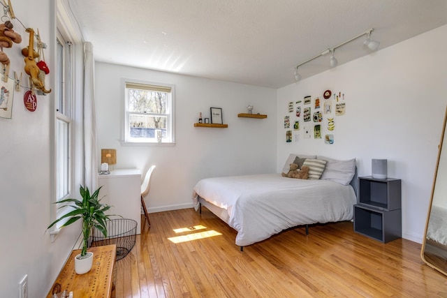 bedroom featuring light wood-style floors, baseboards, and rail lighting