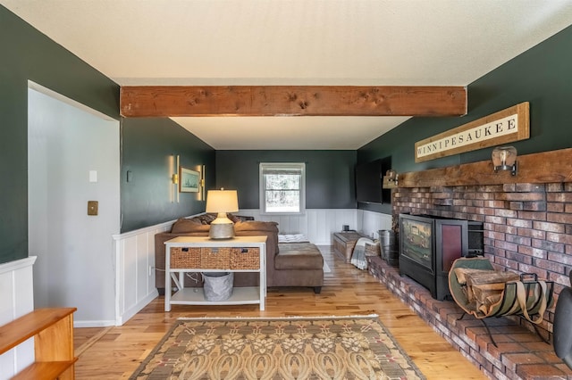living room with a brick fireplace, beam ceiling, a wainscoted wall, and wood finished floors