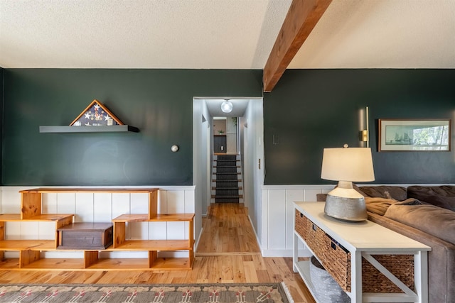 living area with a wainscoted wall, beam ceiling, stairway, and wood finished floors