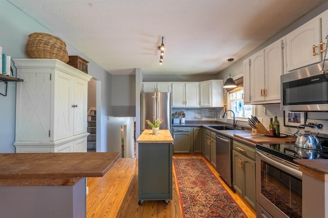 kitchen featuring butcher block countertops, a sink, stainless steel appliances, light wood-type flooring, and white cabinetry