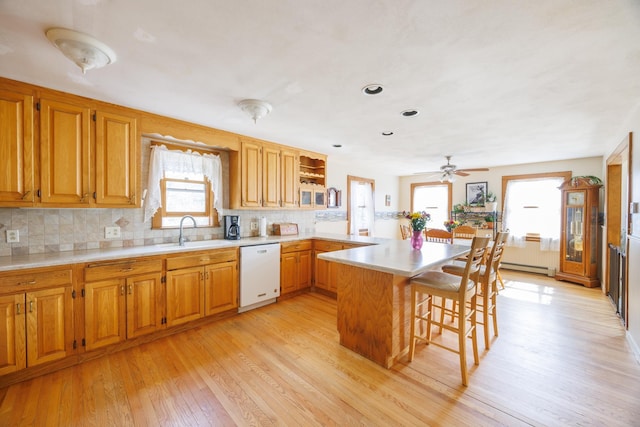 kitchen featuring a peninsula, a breakfast bar area, a sink, light countertops, and white dishwasher
