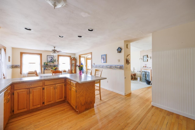 kitchen with light wood-style flooring, a kitchen bar, light countertops, a ceiling fan, and wainscoting