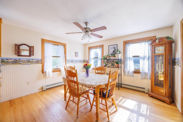 dining space featuring wainscoting, baseboard heating, ceiling fan, and light wood-type flooring