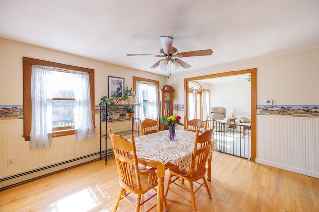dining area featuring a wainscoted wall, light wood-type flooring, a ceiling fan, and a baseboard heating unit