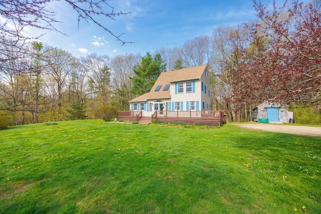 rear view of house with roof with shingles, a wooden deck, an outdoor structure, and a lawn