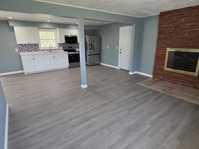 39 Gail St, Winooski, VT 05404 - unfurnished living room with wood finished floors, baseboards, a brick fireplace, and a sink