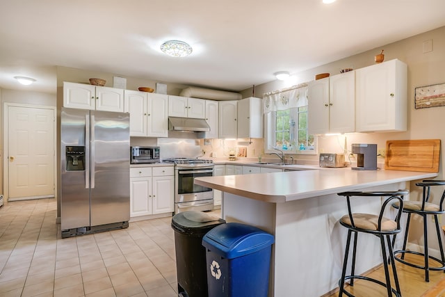 kitchen with a peninsula, a breakfast bar area, stainless steel appliances, white cabinetry, and under cabinet range hood
