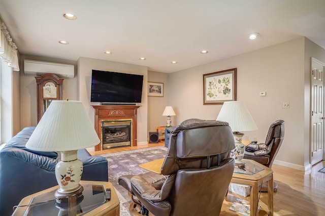 living room featuring a wall unit AC, recessed lighting, baseboards, a glass covered fireplace, and light wood-style floors