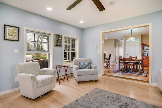 sitting room featuring a baseboard heating unit, ceiling fan, baseboards, and light wood-type flooring