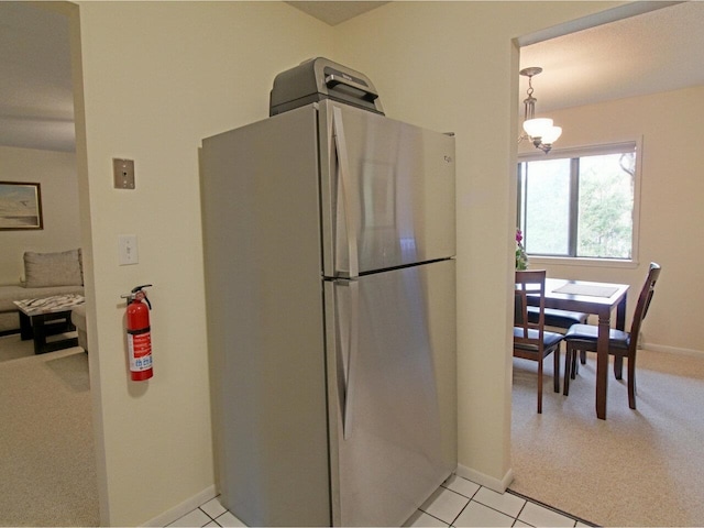 kitchen featuring freestanding refrigerator, baseboards, light colored carpet, a chandelier, and light tile patterned flooring
