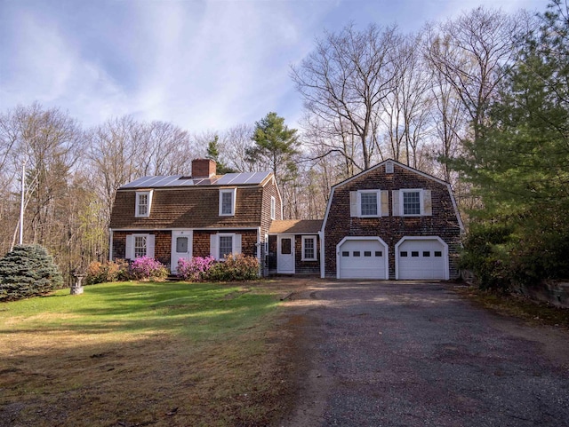 colonial inspired home featuring a chimney, driveway, a gambrel roof, solar panels, and a front yard