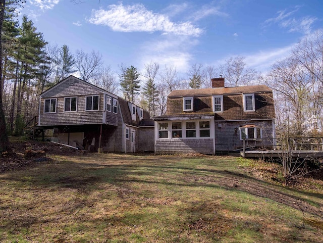 back of house with a gambrel roof, a chimney, a deck, and a lawn