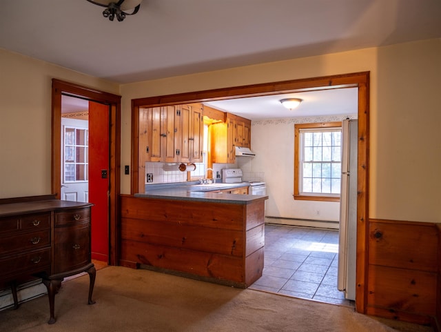 kitchen with a sink, a peninsula, under cabinet range hood, a baseboard radiator, and white range with electric cooktop