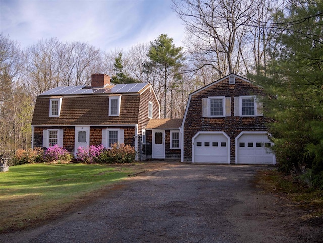 dutch colonial with a gambrel roof, driveway, a front yard, roof mounted solar panels, and a chimney