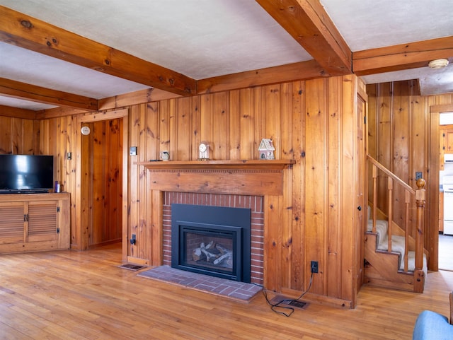 unfurnished living room featuring stairway, wooden walls, beamed ceiling, and wood finished floors
