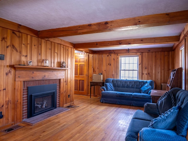 living room with beamed ceiling, light wood finished floors, visible vents, and wood walls