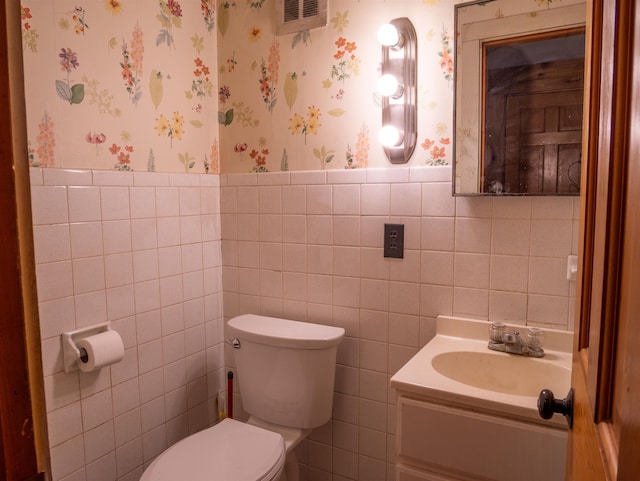 bathroom with toilet, tile walls, wainscoting, and wallpapered walls