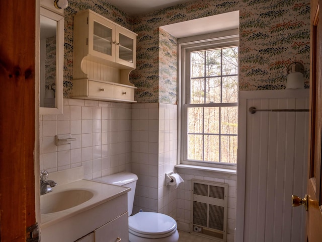 half bathroom featuring a healthy amount of sunlight, tile walls, toilet, and wallpapered walls