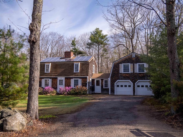 colonial inspired home featuring a chimney, solar panels, a front yard, a gambrel roof, and driveway