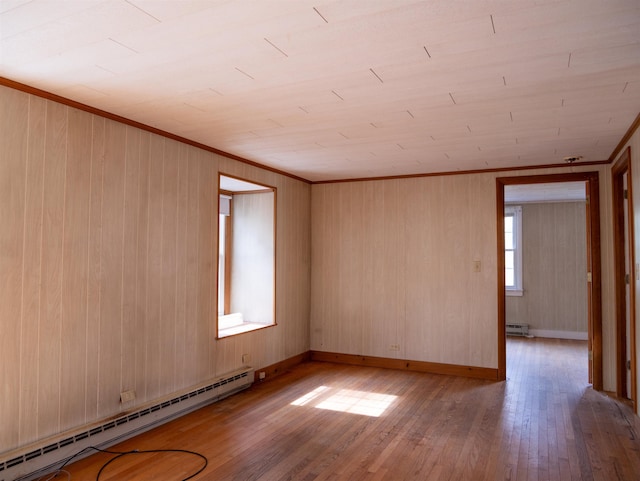 empty room featuring ornamental molding, wood walls, wood finished floors, and a baseboard heating unit