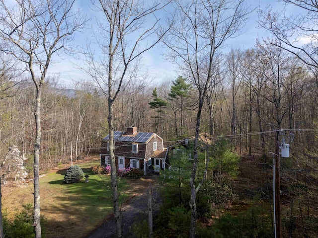 view of front of property with a gambrel roof, a view of trees, a front yard, solar panels, and a chimney