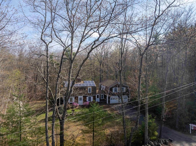 view of front of house with a gambrel roof, roof mounted solar panels, driveway, and a view of trees