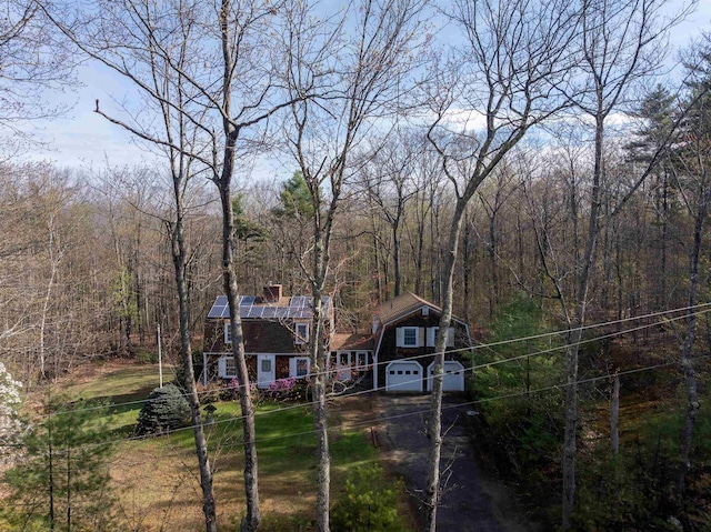 view of front facade with an attached garage, a forest view, a chimney, and driveway