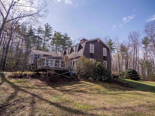 rear view of house with a chimney, a lawn, a wooden deck, stairway, and a gambrel roof
