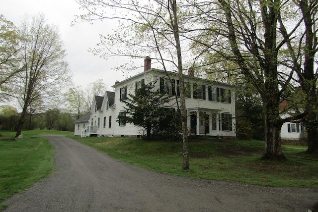view of front of home featuring a front lawn, dirt driveway, and a chimney