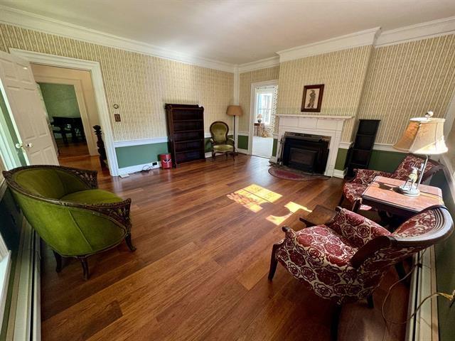 living area featuring wallpapered walls, wood finished floors, a fireplace, and crown molding