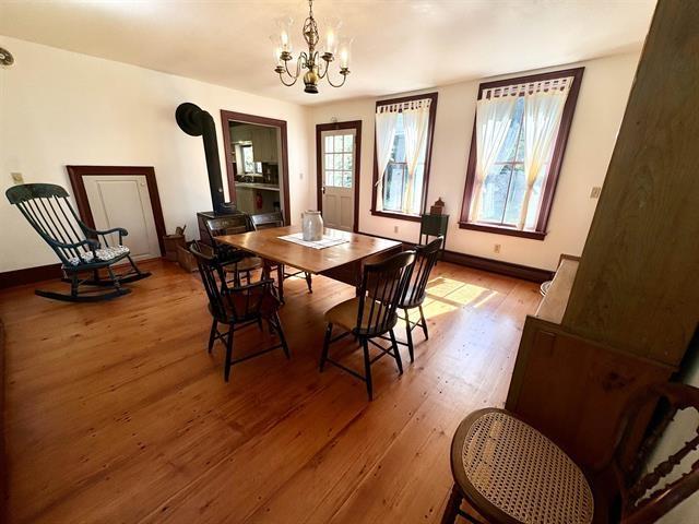 dining space featuring light wood finished floors, a wood stove, baseboards, and a notable chandelier