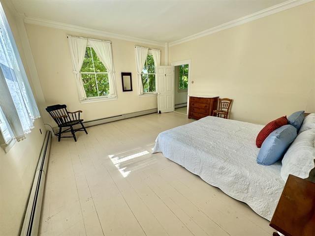 bedroom featuring crown molding, wood finished floors, a baseboard radiator, and a baseboard heating unit