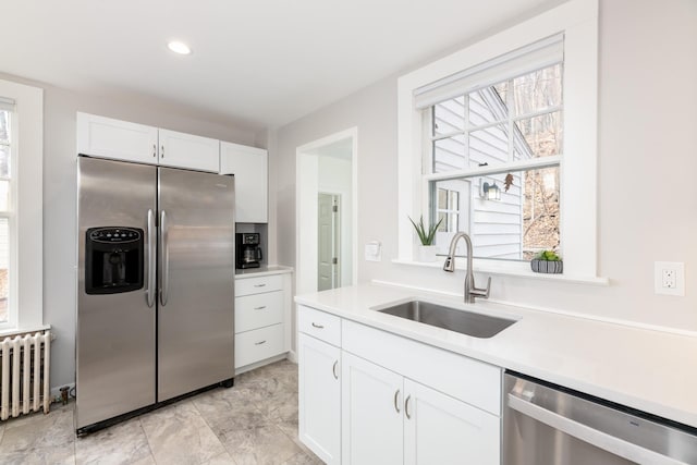 kitchen with a sink, radiator, light countertops, white cabinets, and appliances with stainless steel finishes