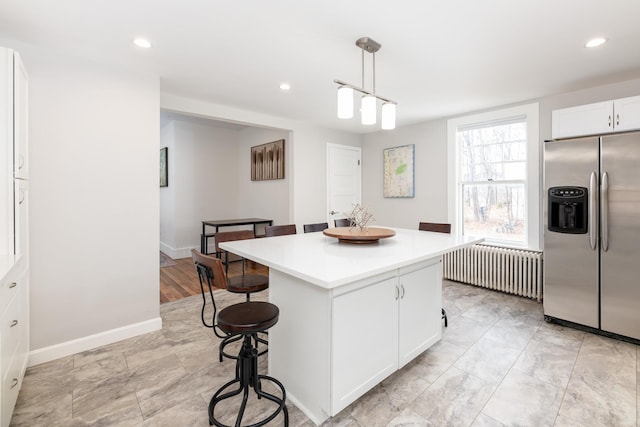 kitchen featuring a center island, a breakfast bar, radiator heating unit, white cabinetry, and stainless steel fridge with ice dispenser