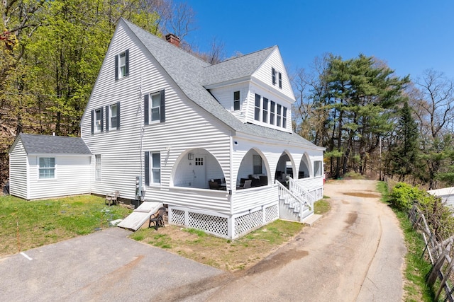 view of front of home featuring driveway, a porch, roof with shingles, and a chimney
