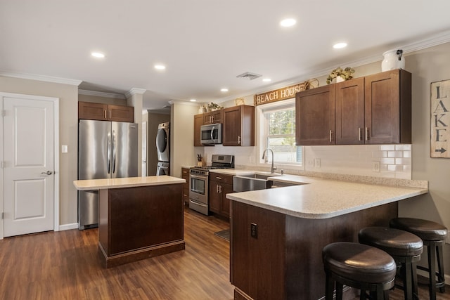 kitchen with a sink, a kitchen breakfast bar, stacked washer and clothes dryer, light countertops, and appliances with stainless steel finishes
