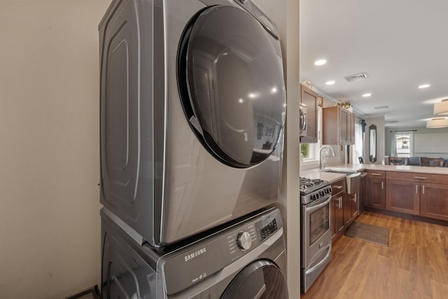 laundry area with recessed lighting, visible vents, a sink, light wood-style floors, and stacked washer / drying machine