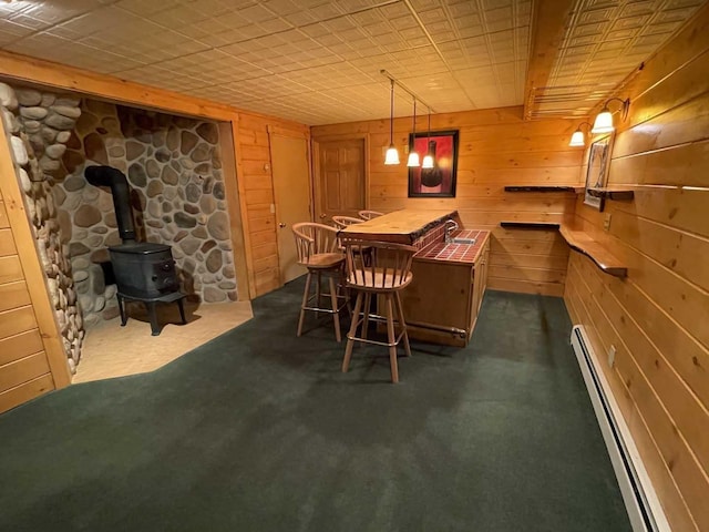 dining space featuring a wood stove, wooden walls, dark carpet, and a baseboard heating unit