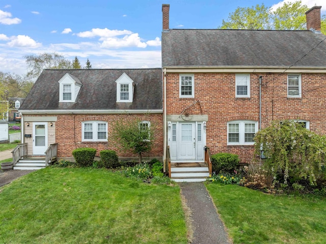 view of front of house with a front lawn, brick siding, a chimney, and entry steps