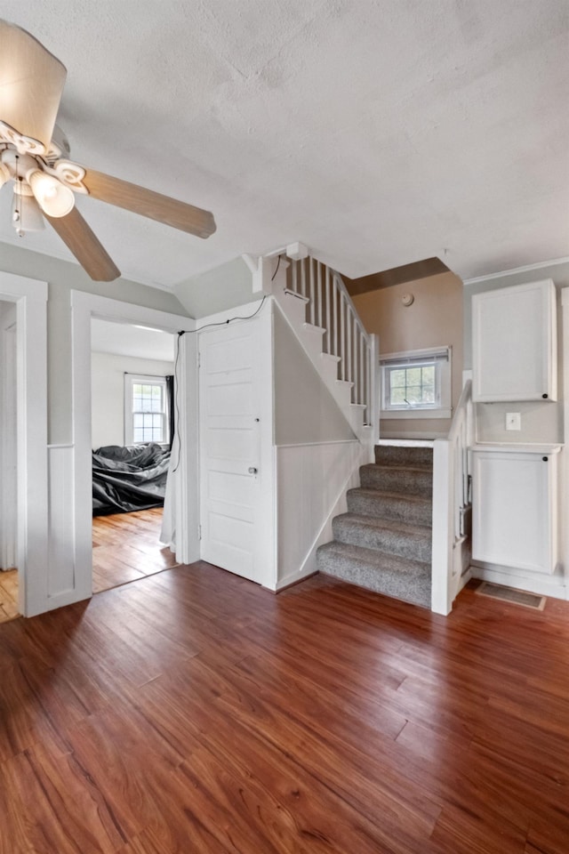 unfurnished living room with ceiling fan, stairs, plenty of natural light, and wood finished floors